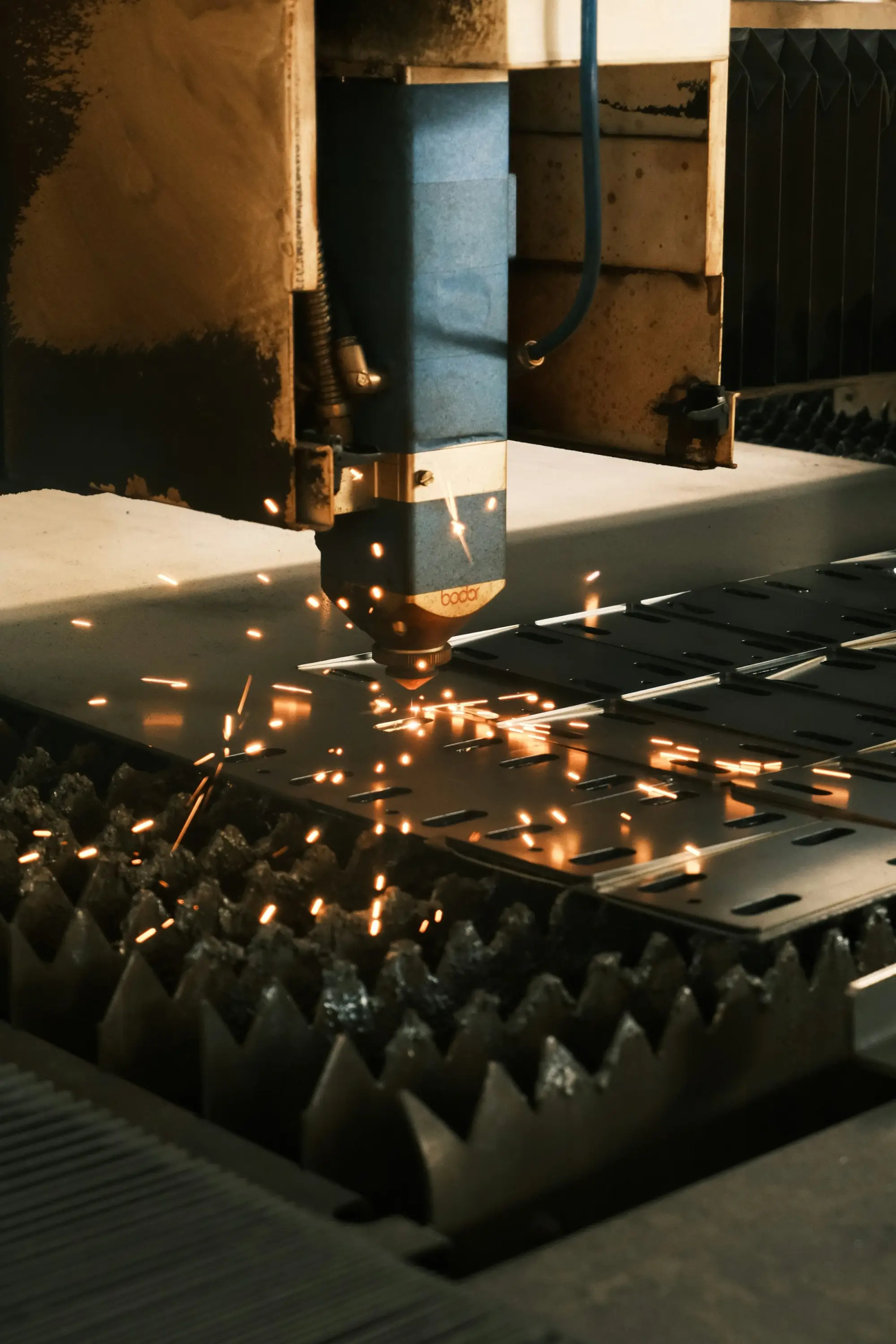 Industrial laser cutting machine cutting a sheet of metal with sparks flying.