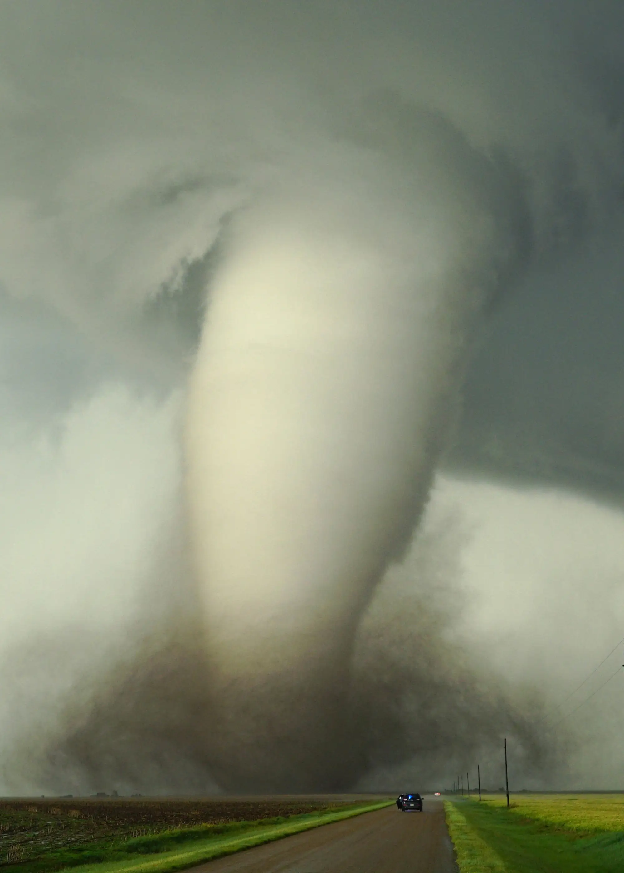 Large tornado crossing farmland near a rural road under dark storm clouds.